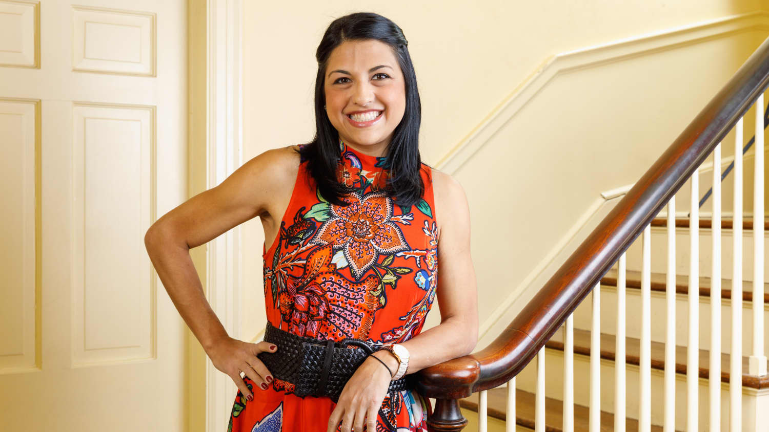 Amanda wearing a patterned red dress leans on a bannister. 